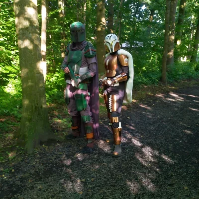 Zwei Personen in detailreichen Rüstungen und Helmen stehen auf einem Waldweg umgeben von Bäumen