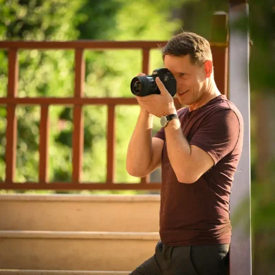 Fotograf Alexander Konopka hält eine Kamera vor sein Gesicht und macht ein Foto im Freien