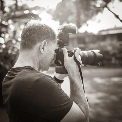 Alexander Konopka hält Kamera mit großem Objektiv und Blitzgerät im Freien und fotografiert