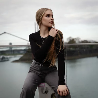 Model Anastasiia mit langem Haar und schwarzem Oberteil sitzt vor einem Geländer am Rhein in Düsseldorf.