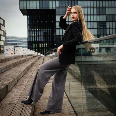 Model mit langen blonden Haaren lehnt auf einer Glasbrüstung neben einer Treppe im Medienhafen – urbane Bildstimmung.