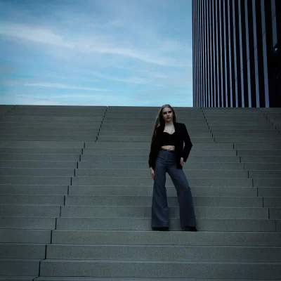 Model Anastasiia mit langen Haaren und dunkler Kleidung steht auf breiter Treppe am Hotel Hyatt Regency Düsseldorf während des Fotoshootings