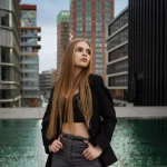 Model Anastasiia Bondarchuk trägt bauchfreie schwarze Korsage und schwarzen Blazer steht vor einem Wasserbecken im Medienhafen Düsseldorf bei einem urbanen Shooting