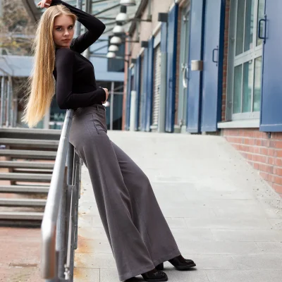 Model Anastasiia mit langen, glatten Haaren lehnt in weiter Hose und langärmligem Oberteil an einem Geländer vor einem modernen Gebäude bei einem TFP-Fotoshooting in Düsseldorf