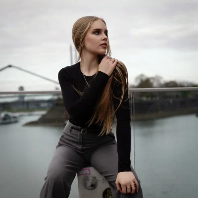 Model Anastasiia mit langem Haar und schwarzem Oberteil sitzt vor einem Geländer am Rhein in Düsseldorf.