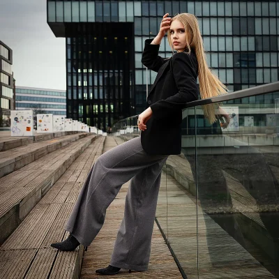 Model mit langen blonden Haaren lehnt auf einer Glasbrüstung neben einer Treppe im Medienhafen