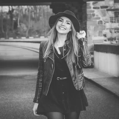 Weibliches Model mit langem Haar, das in einer Lederjacke und einem Hut lächelnd auf der Möhnesee-Staumauer posiert.