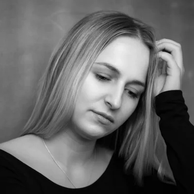 Weibliches Model mit langen Haaren schaut nach unten, Hand an Kopf, Schwarz-Weiß-Porträtaufnahme im Indoor-Fotoshooting
