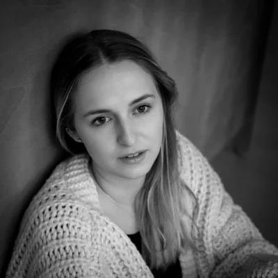 Porträt einer entspannt blickenden Frau mit langem Haar in einem grob gestrickten Pullover vor neutralem Hintergrund