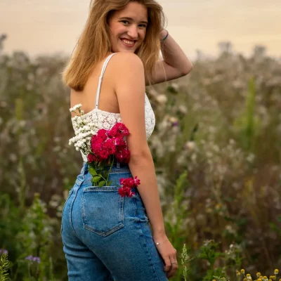 Frau mit Blumen in der Tasche vor Feld schaut über Schulter