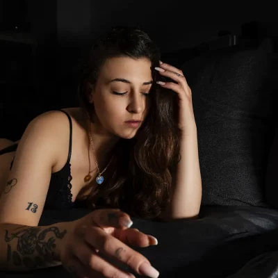 Frau mit langen dunklen Haaren und Tattoos am Arm liegt mit geschlossenen Augen auf schwarzem Sofa