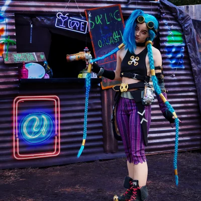 League-of-Legends-Cosplayerin mit sehr langen blauen Zöpfen und Crop-Top an einer Endzeit-Bar mit Neon- und Kreidetafel-Schildern