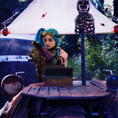 Cosplaymodel mit langer blauer Zopfperücke und Steampunk-Brille hält eine große Fantasy-Waffe, neben einer Totenkopf-Attrappe.