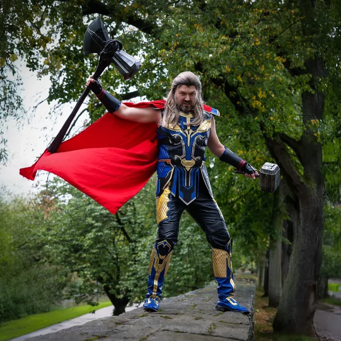 Chris in Thor-Kostüm mit rotem Umhang steht auf der Stadtmauer und hält zwei Hämmer in erhobenen Händen; Cosplay-Fotoshooting
