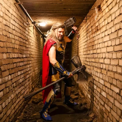 Kyurocosplay mit rotem Umhang und Hammer posiert kämpferisch in einem engen, beleuchteten Ziegelgang