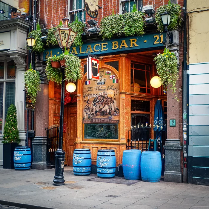 Außenansicht der Palace Bar in Dublin mit hölzernen Fassaden, blauen Barrels und grünen Pflanzen an der Fassade
