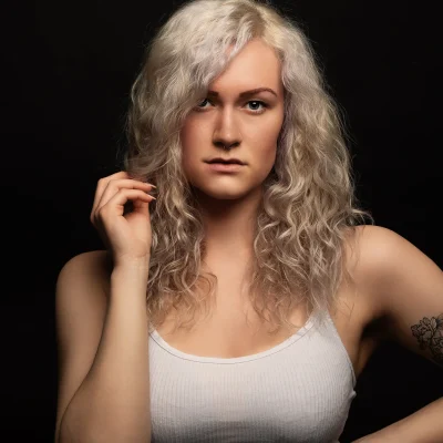 Weibliches Model mit lockigen blonden Haaren, das ernst in die Kamera schaut und ein weißes ärmelloses Top trägt.