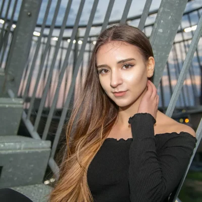 Junge Frau mit langen Haaren in schwarzem, schulterfreiem Oberteil auf einer Metalltreppe des Tiger and Turtle Monuments bei Dämmerung