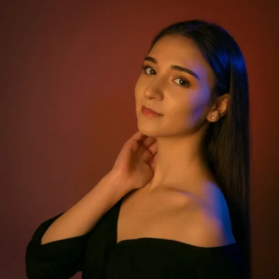 Portrait des Models Gamze Kuva mit schulterfreiem schwarzen Oberteil und zurückgekämmtem Haar vor rotem Hintergrund mit Blaulichtakzenten