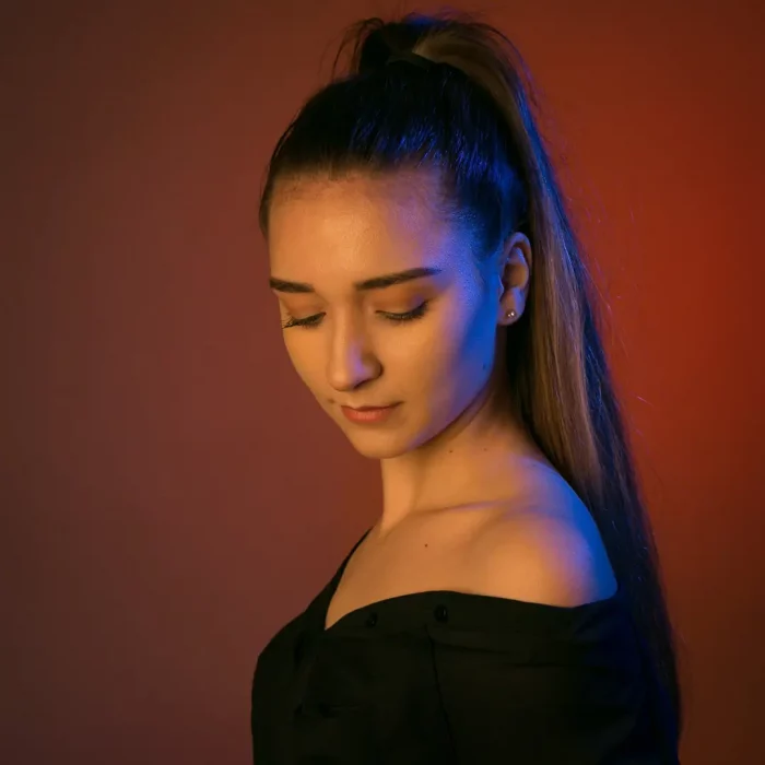 Portraitfoto eines weiblichen Models mit schwarzem schulterfreiem Top, das den Kopf nach unten neigt, vor einfarbigem rotem Hintergrund
