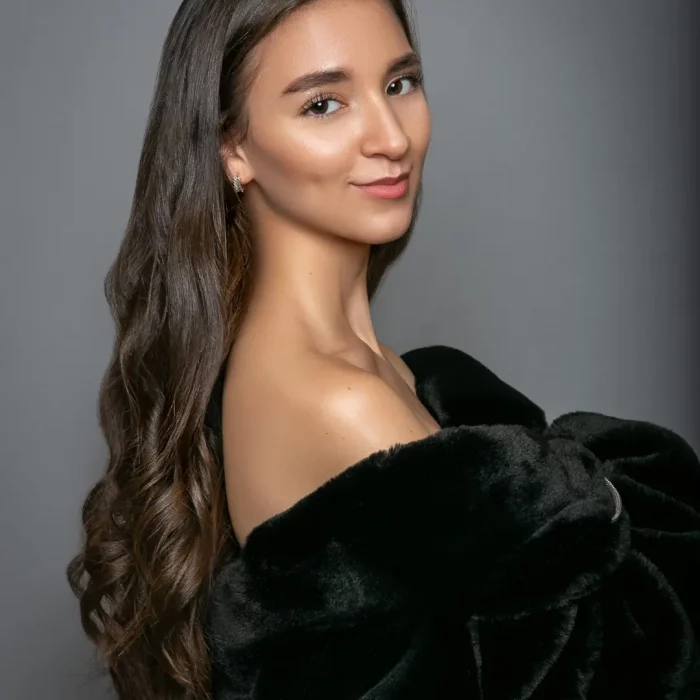 Portraitfoto des Models Gamze Kuva mit schwarzem langem gewelltem Haar und schwarzem Fellmantel, die über die unbedeckte Schulter blickt