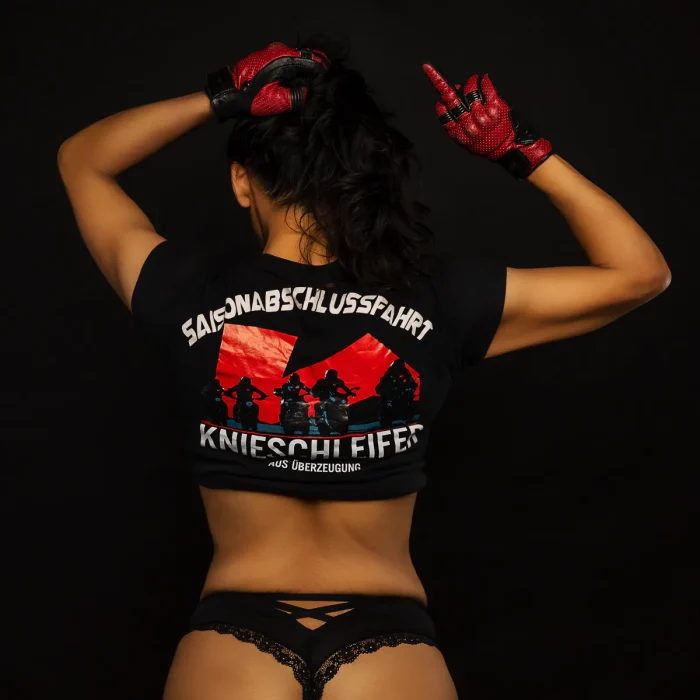 Model Hani von hinten in schwarzer Spitzenunterwäsche und kurzem Shirt mit roten Motorradmotiven, Model zeigt den Mittelfinger.