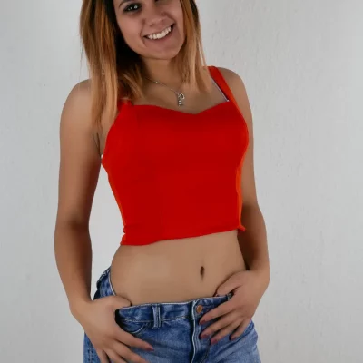 Porträtfotografie einer jungen Frau mit rotem Top und blauen Jeansshorts vor weißem Hintergrund, freier Oberkörper, lächelnder Gesichtsausdruck