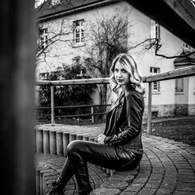 Portraitfotografie einer Frau in schwarzer Lederjacke und Lederhose, sitzend auf einer Rundbank im Freien, schwarz-weiß aufgenommen