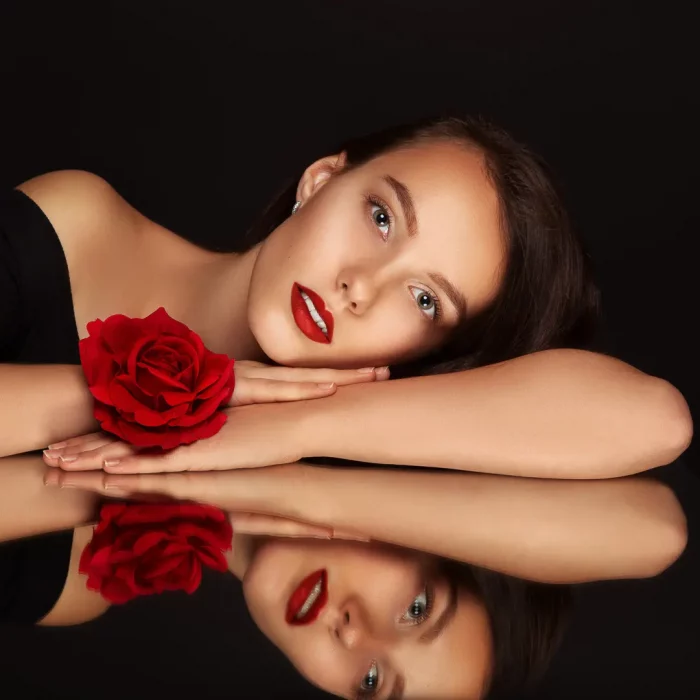 TFP-Fotoshooting in NRW mit Spiegel: Model Jennifer mit roter Rose am Handgelenk und rotem Lippenstift, deren Gesicht sich auf einer glänzenden Oberfläche spiegelt.