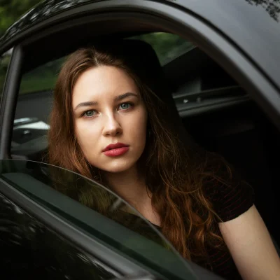 Portraitfotografie einer jungen Frau mit langen braunen Haaren, die aus einem geöffneten Autofenster schaut