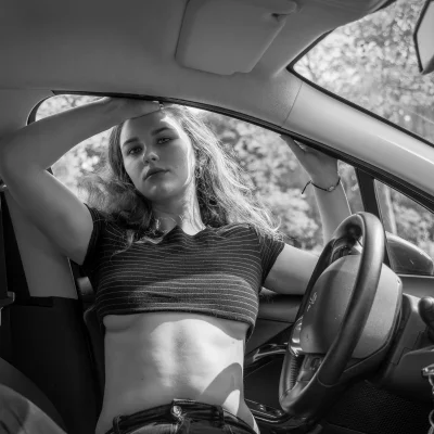 Frau in geringeltem Crop-Top lehnt mit erhobenem Arm lässig aus Autofenster
