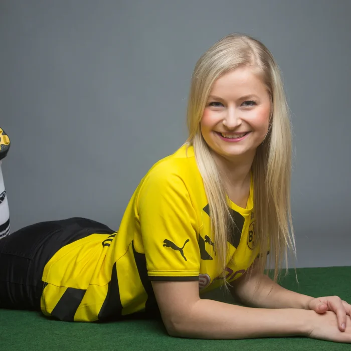 Lächelnde Frau liegt auf dem Bauch auf grünem Untergrund trägt gelb-schwarzes Fußballtrikot und weiße Sportsocken mit schwarzen Streifen