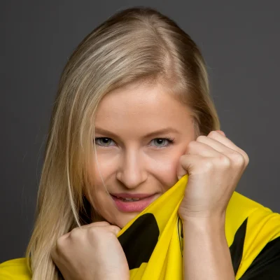 Model Jessica hält ihr gelbes und schwarzes Trikot mit beiden Händen vor das Gesicht und lächelt