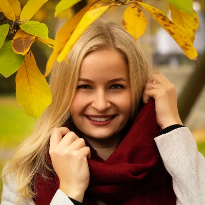 Junge Frau mit blonden Haaren unter gelben Herbstblättern, Herbst Fotoshooting mit rotem Schal und hellem Mantel