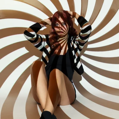 Weibliches Model in sitzender Pose vor einer rotierenden Spiralmuster-Projektion, kontrastreiche Licht- und Schattenspiele auf Haut und Kleidung