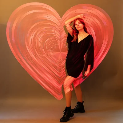 Junges weibliches Model steht in Schwarz gekleidet vor großem, leuchtend rotem Herz als zentrales Element eines künstlerischen Portraitshootings.