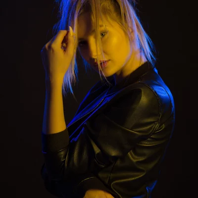 Model KA_TE mit hochgestecktem Haar trägt eine schwarze Lederjacke und hält eine Hand an den Kopf.