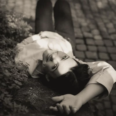 Frau liegt auf Mauer mit Kopfsteinpflaster im Hintergrund und blickt lächelnd zur Kamera