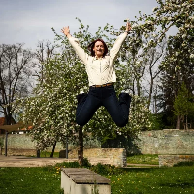 Model Katarina springt mit ausgestreckten Armen und Beinen vor einem blühenden Baum in der Nähe vom Mitmachgarten in Soest
