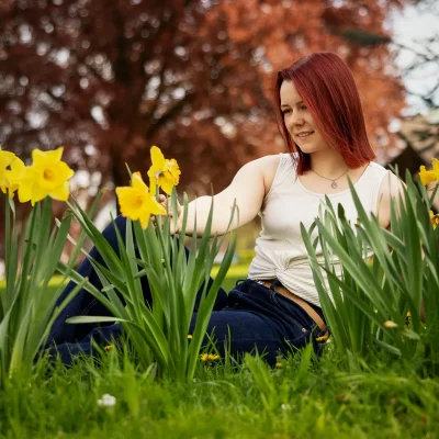 Frau mit roten Haaren sitzt auf einer Wiese zwischen gelben Narzissen