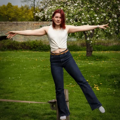Katarina mit weißem ärmellosem Oberteil und blauen Jeans balanciert mit ausgestreckten Armen auf einer Slackline in den Gräften von Soest