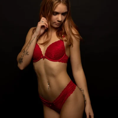 Dessous-Shooting mit Kathi in Soest: Rote Spitzenunterwäsche mit sichtbaren Tattoos an beiden Armen vor schwarzem Hintergrund
