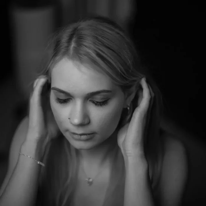 Schwarz-weißes Portraitfotografie eines weiblichen Models mit gesenktem Blick und beiden Händen am Kopf