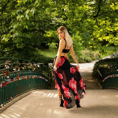 Frau mit langem blonden Haar, schwarzem Oberteil und geblümtem Rock steht auf Brücke im Park und blickt über die Schulter zurück - Portrait Fotoshooting in Dortmund.
