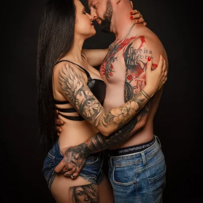 Paar mit sichtbaren Tattoos auf Armen und Oberkörpern umarmt sich eng und küsst sich, beide in Unterwäsche oder knapper Kleidung