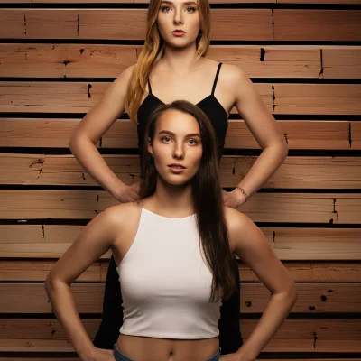 Klaudia und Jennifer stehen frontal vor einer vertikal ausgerichteten Holzwand, beide mit ernstem Blick.