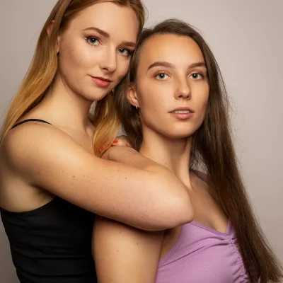 Freundinnen Fotoshooting: Klaudia und Jennifer stehen eng beieinander, Klaudia umarmt Jennifer von hinten, beide tragen ärmellose Oberteile.
