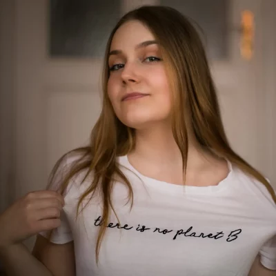 Frau mit langen, offenen Haaren, weißem T-Shirt und dem schwarzen Aufdruck „there is no planet B“, unscharfer Hintergrund