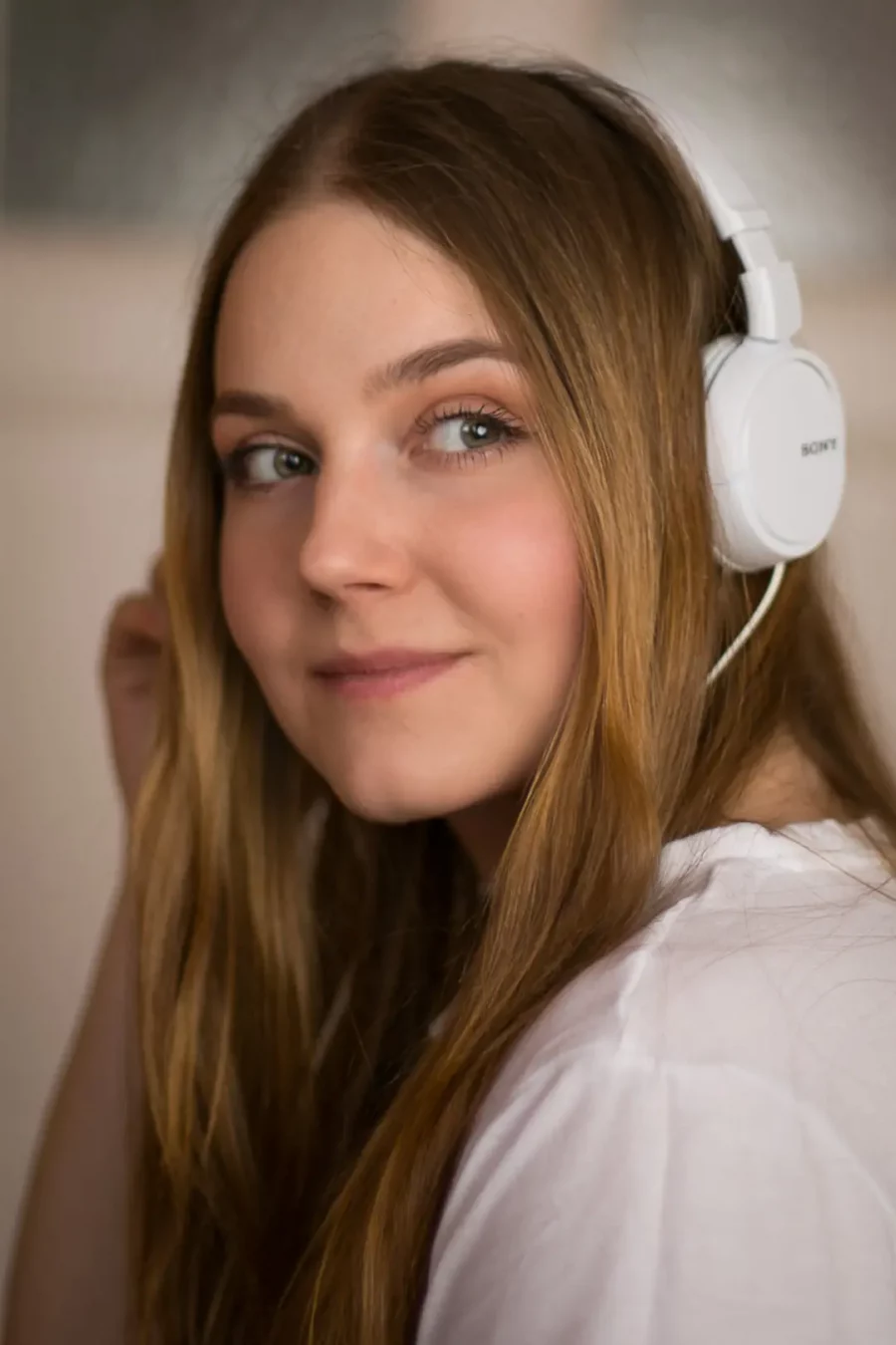 Porträtfotografie von Laura mit langen blonden Haaren, die weiße Kopfhörer trägt und über die Schulter blickt.