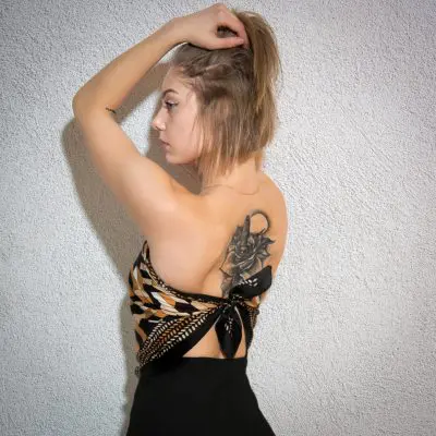 Frau mit Tattoo auf dem Rücken seteht vor Wand